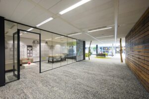Modern office interior at Jacob Bontiusplaats with glass meeting rooms, cozy lounge areas, and wood-paneled and carpeted design elements.